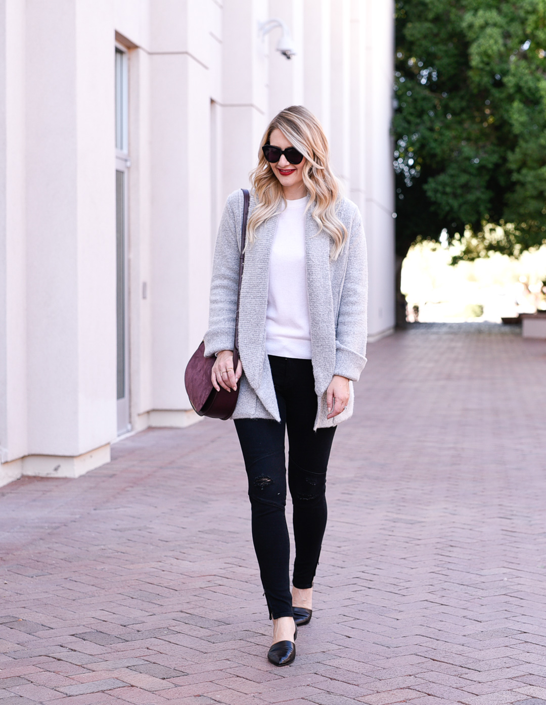 Jenna Colgrove wearing fall essentials: grey cardigan, black distressed denim, and a burgundy leather crossbody bag 