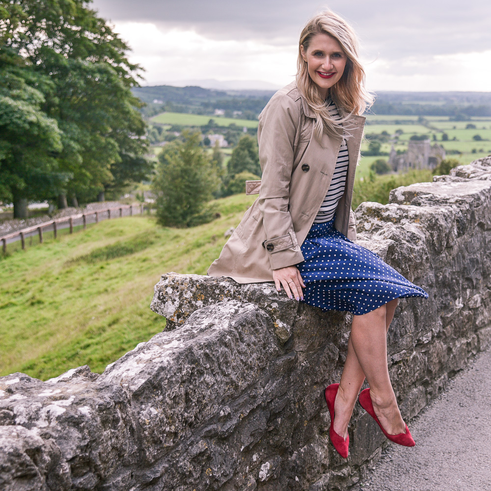 Jenna Colgrove in a J.Crew polka dot dress and London Fog trench coat at Rock of Cashel, Ireland. 