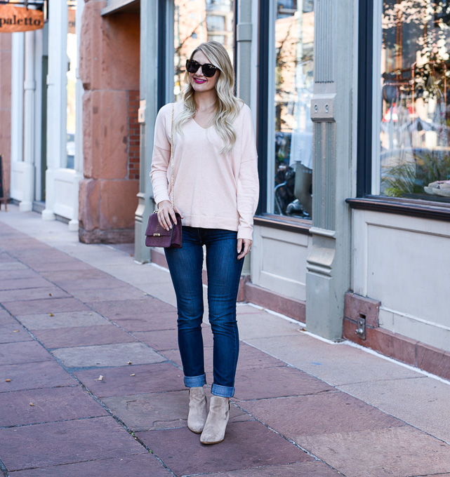 Jenna Colgrove wearing a pink sweater, dark wash jeans, and beige booties in Lodo, Denver. 