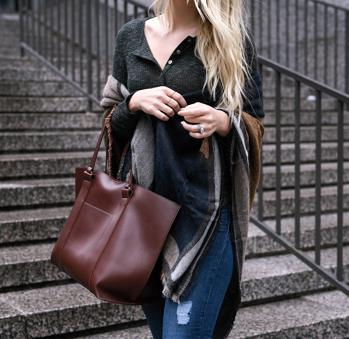 Jenna Colgrove wearing a dark green henley, distressed denim, and a navy shawl. 