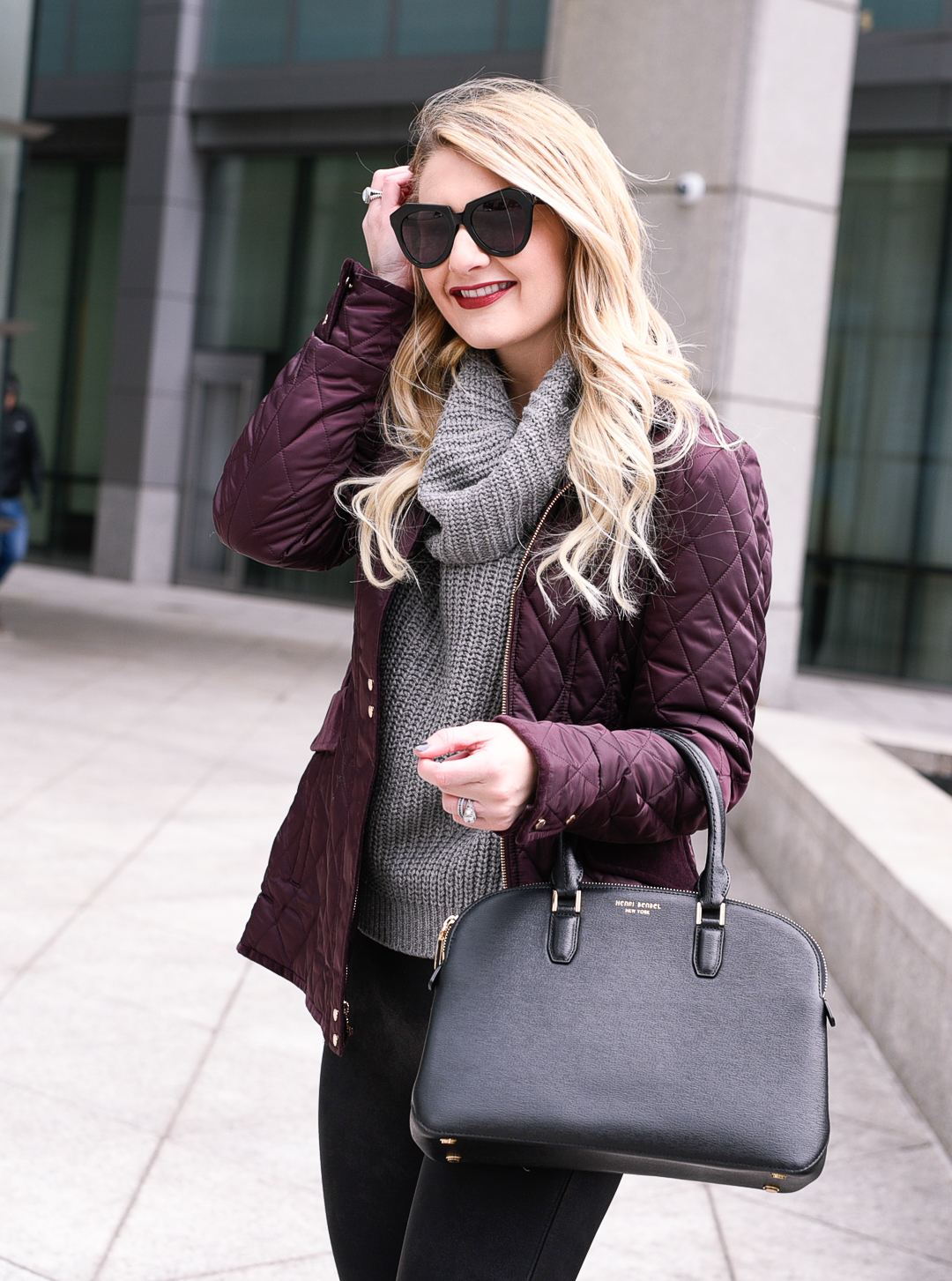 Jenna Colgrove wearing the Henri Bendel Dome Satchel, a Vince Camuto purple jacket, and a grey knit turtleneck. 