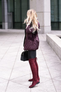 Jenna Colgrove wearing a wine colored quilted coat, black leather pants, and otk boots.
