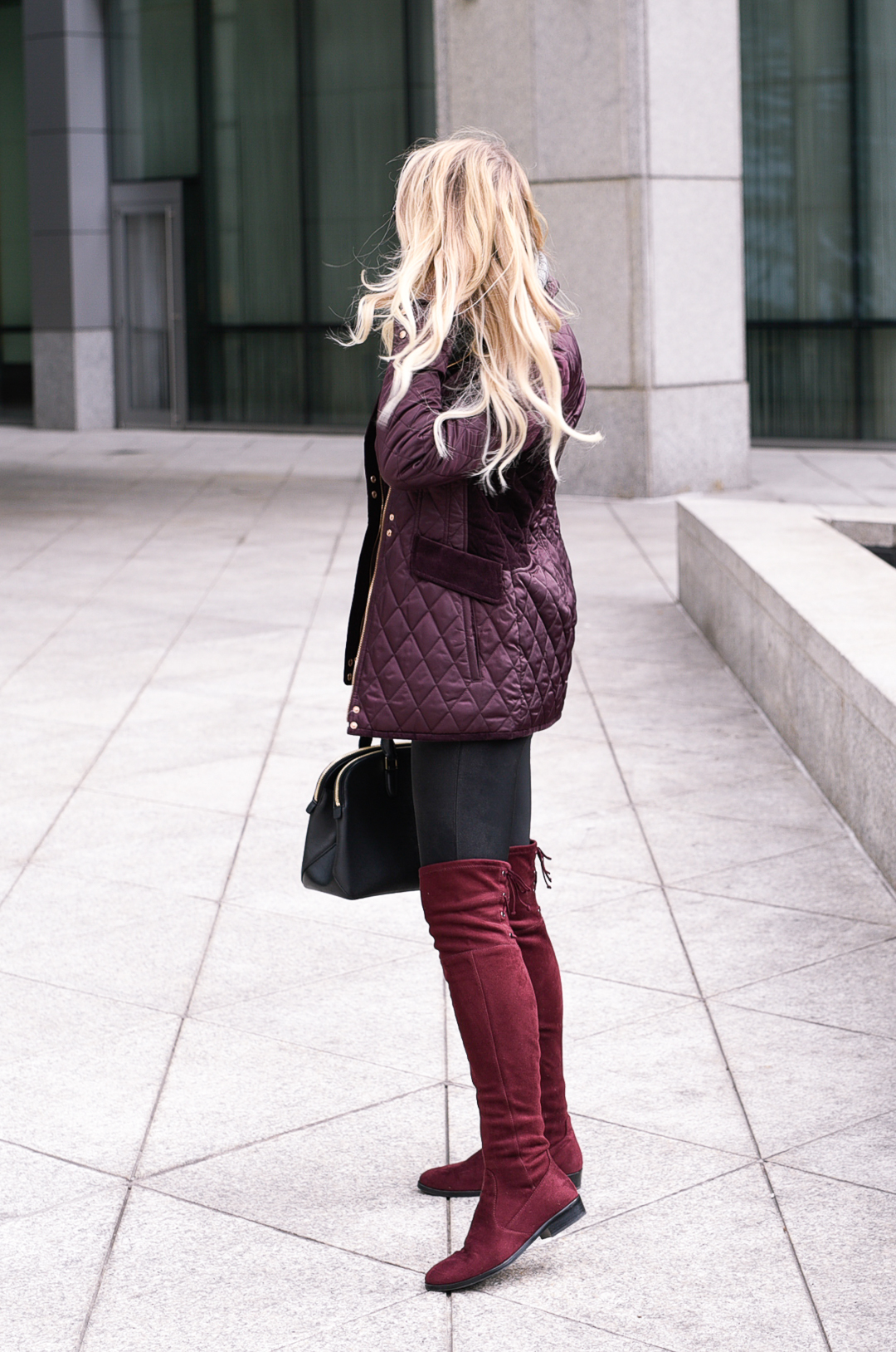 Jenna Colgrove wearing a wine colored quilted coat, black leather pants, and otk boots. 