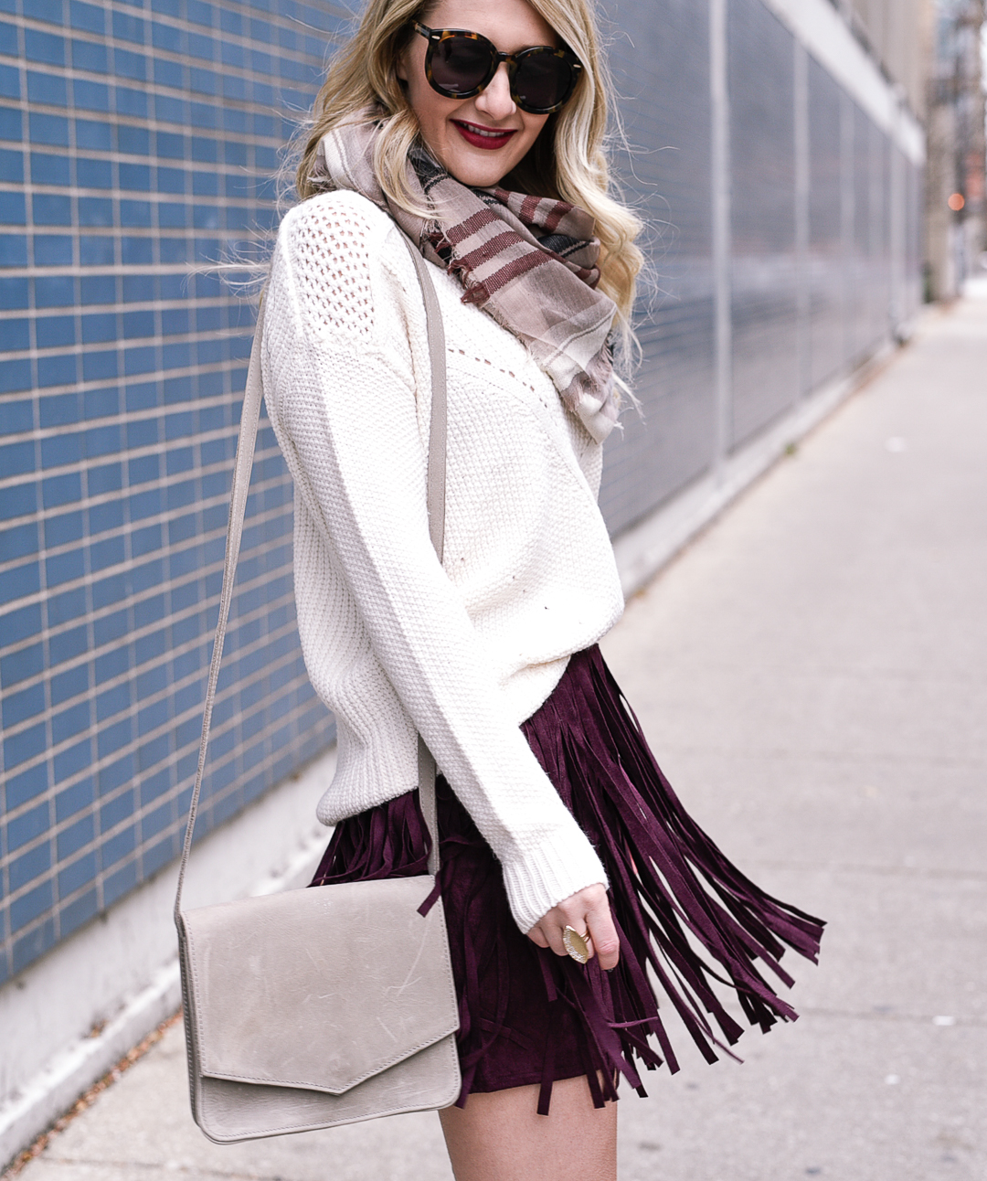 Jenna Colgrove wearing a cozy white knit sweater and a burgundy fringe mini skirt. 