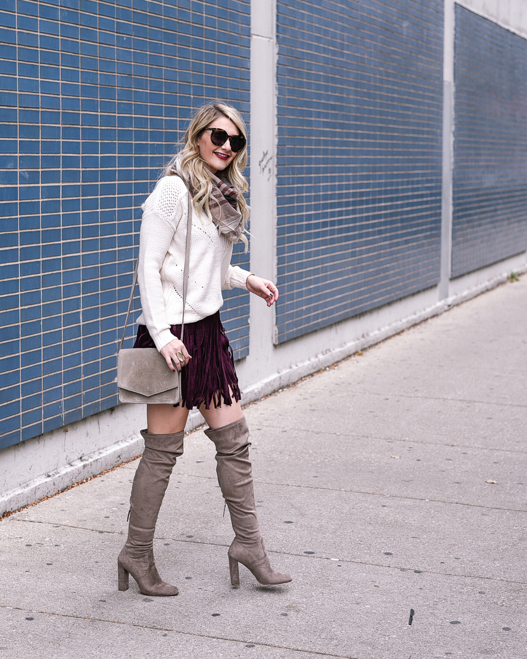 Jenna Colgrove wearing an ivory sweater, burgundy fringe suede skirt, and taupe otk boots. 
