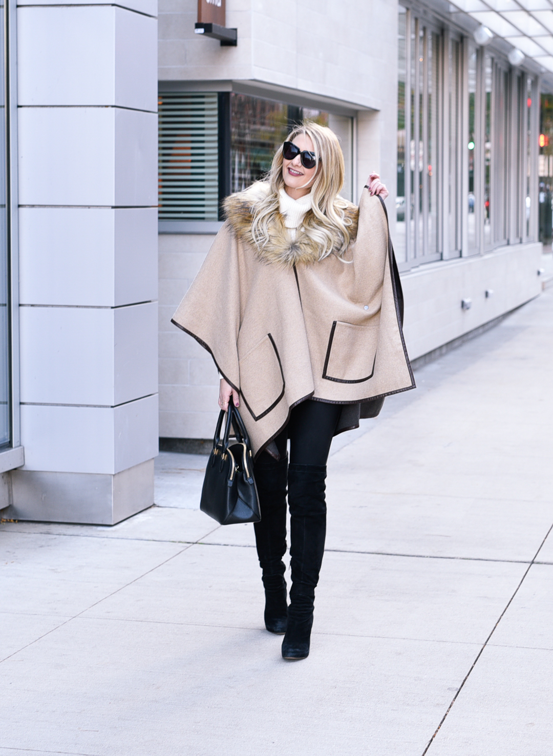 Jenna Colgrove wearing a beige cape, black leather leggings, and suede over the knee boots. 