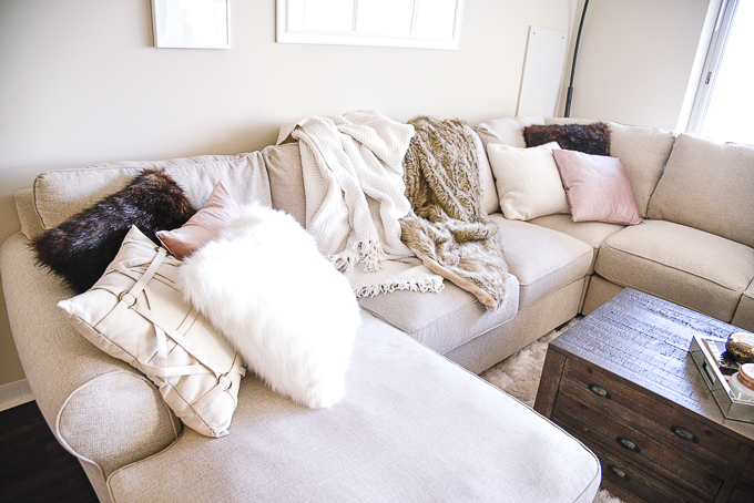 Mixing textures with faux fur pillows, knit blankets, and linen fabrics in a trendy living room redesign. 