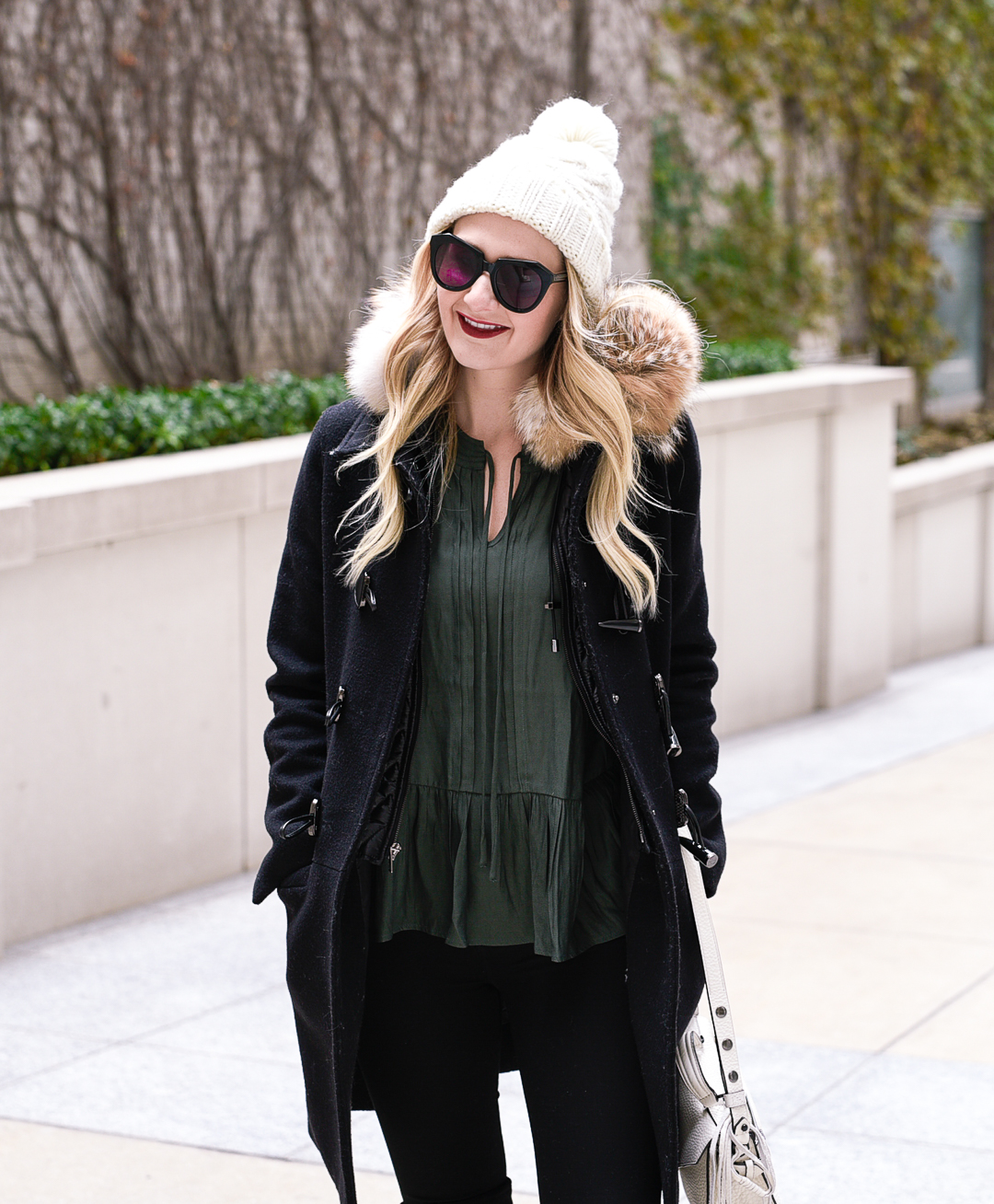 White beanie, dark green blouse, and a black wool winter coat. 