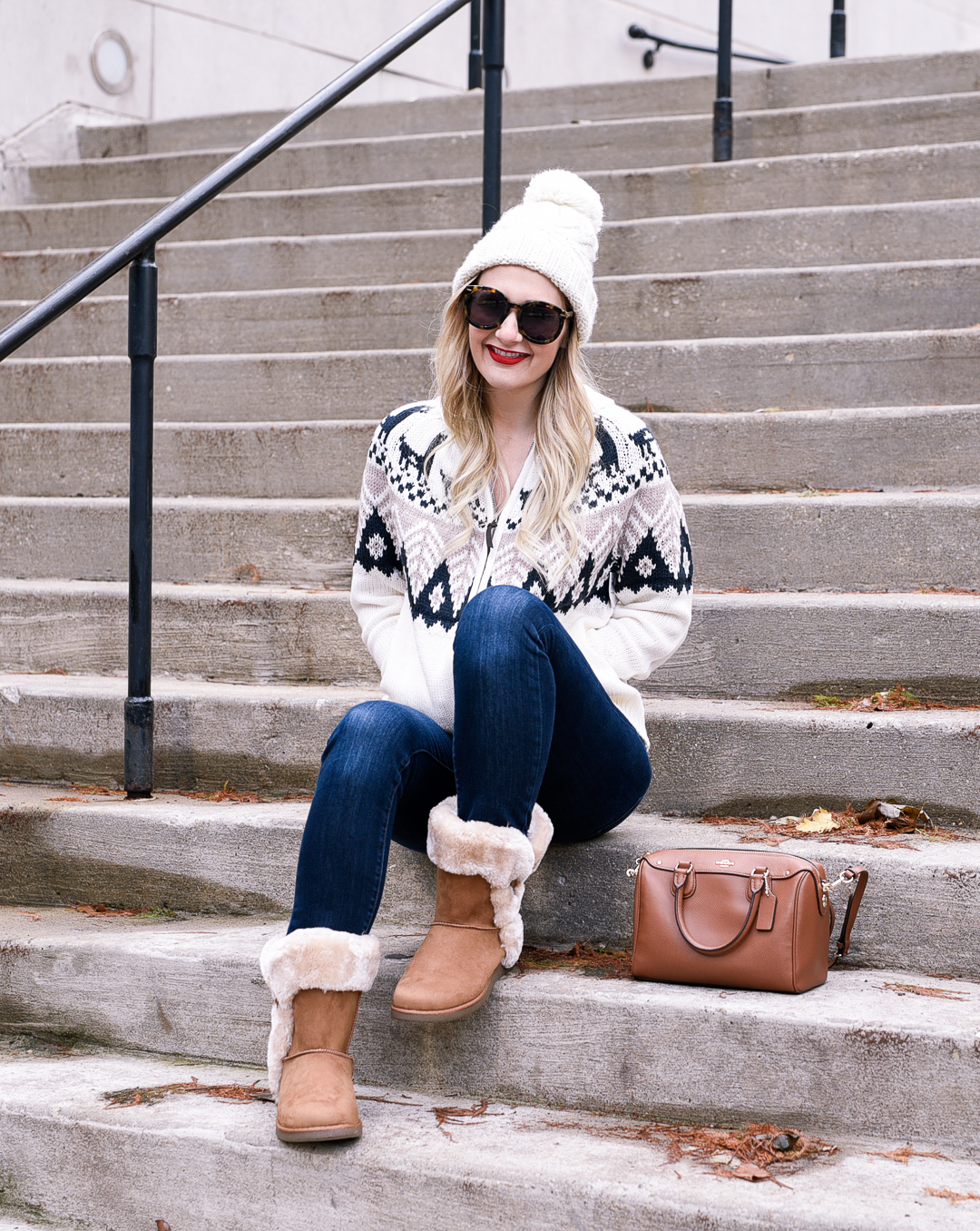 Jenna Colgrove wearing a white beanie, knit sweater, and dark wash denim jeans. 