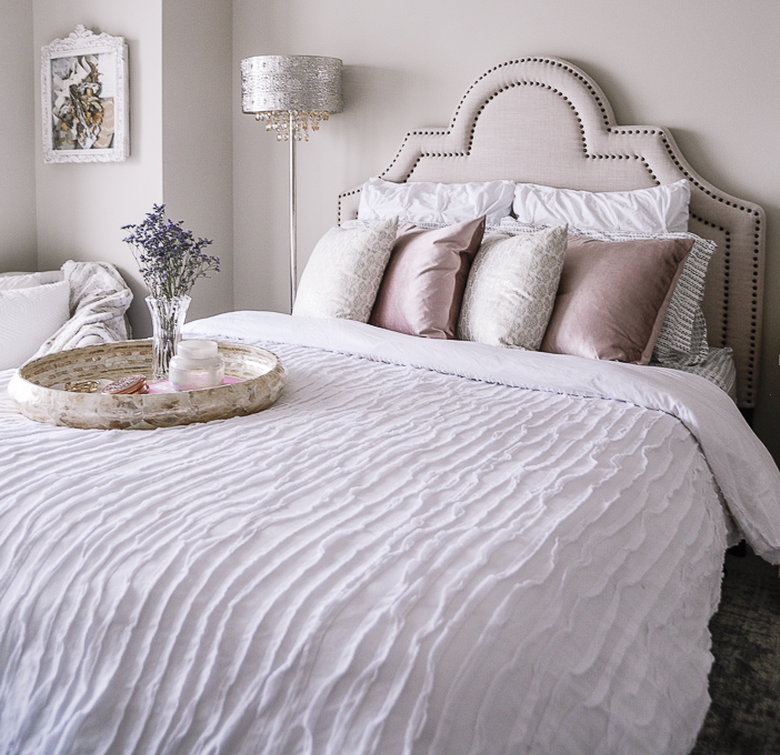 A white ruffled bedspread and pink velvet pillows.