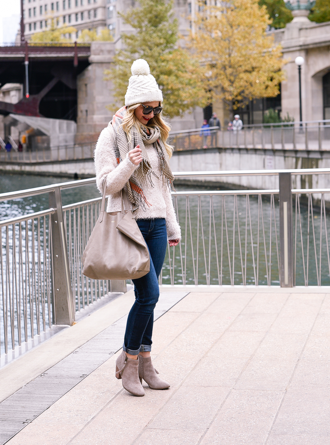 Jenna Colgrove wearing a plaid blanket scarf, taupe booties, and a fuzzy white turtleneck. 