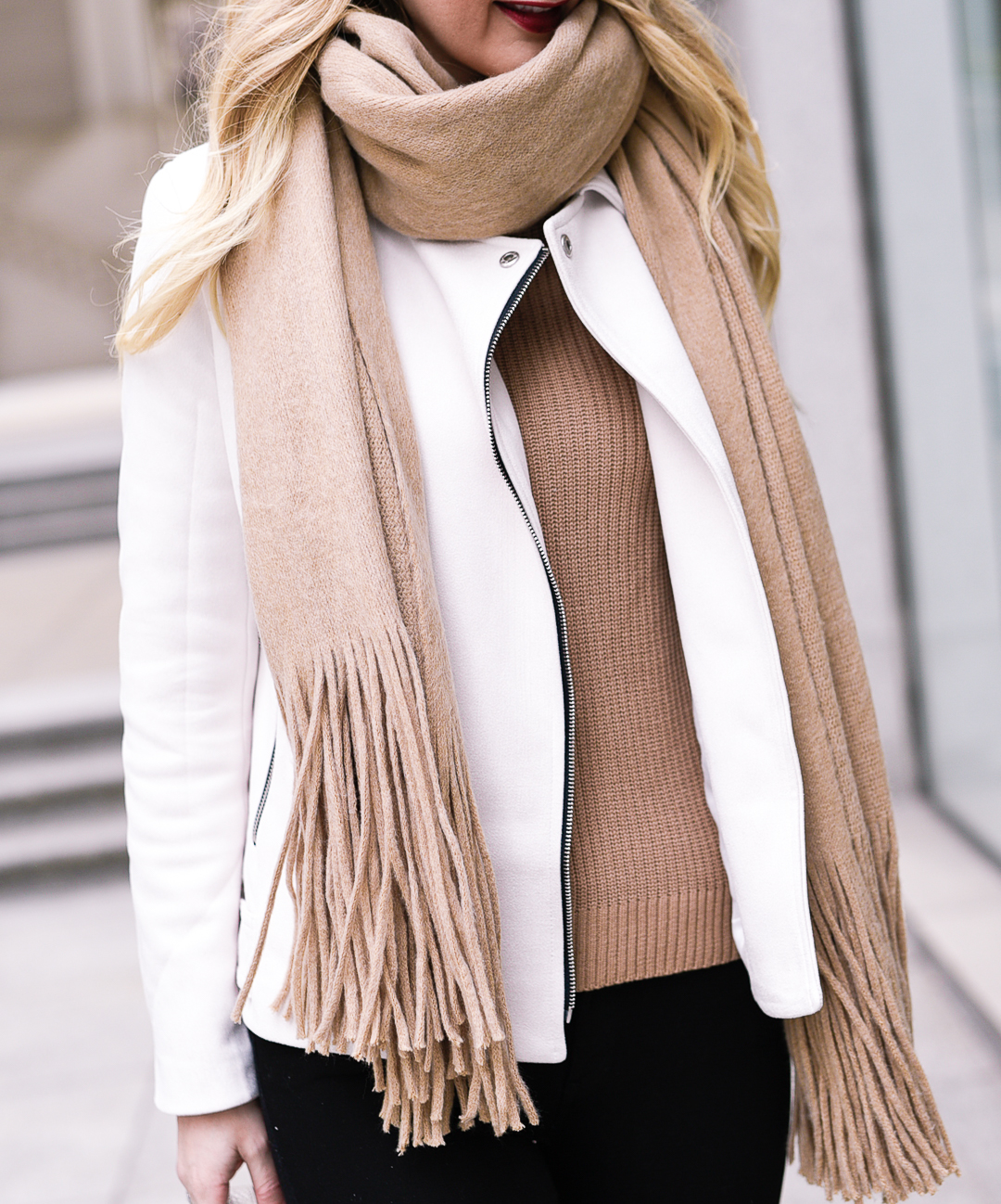 Camel fringe scarf, white moto jacket, and beige sweater. 