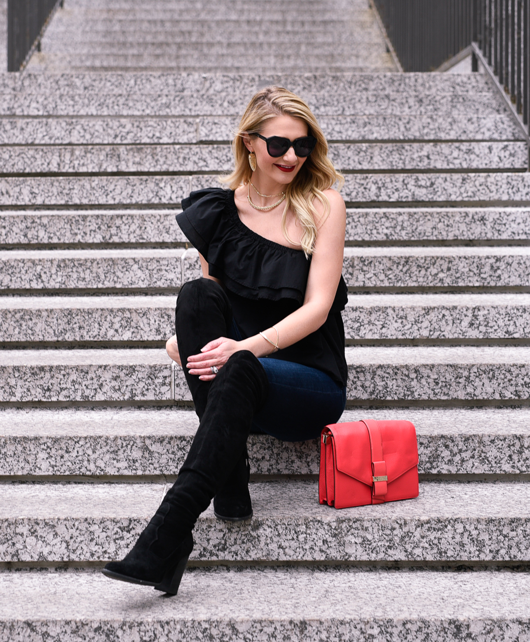 Black suede boots, red statement clutch, and a black ruffled top. 