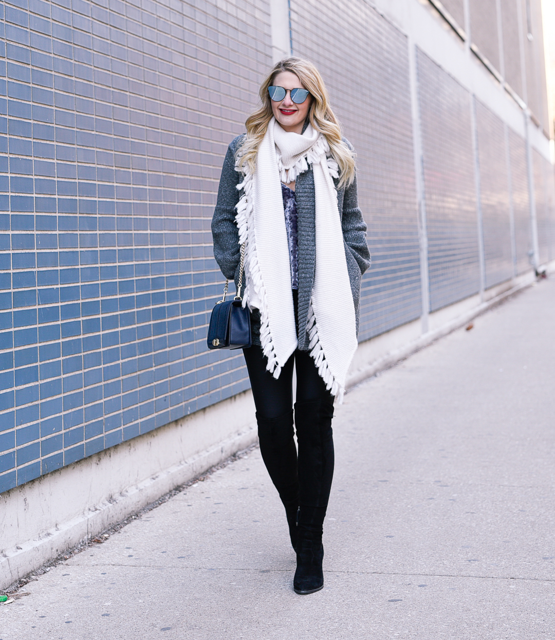 Jenna Colgrove wearing a blue velvet Rebecca Minkoff crossbody bag and a tear drop sleeve grey cardigan. 