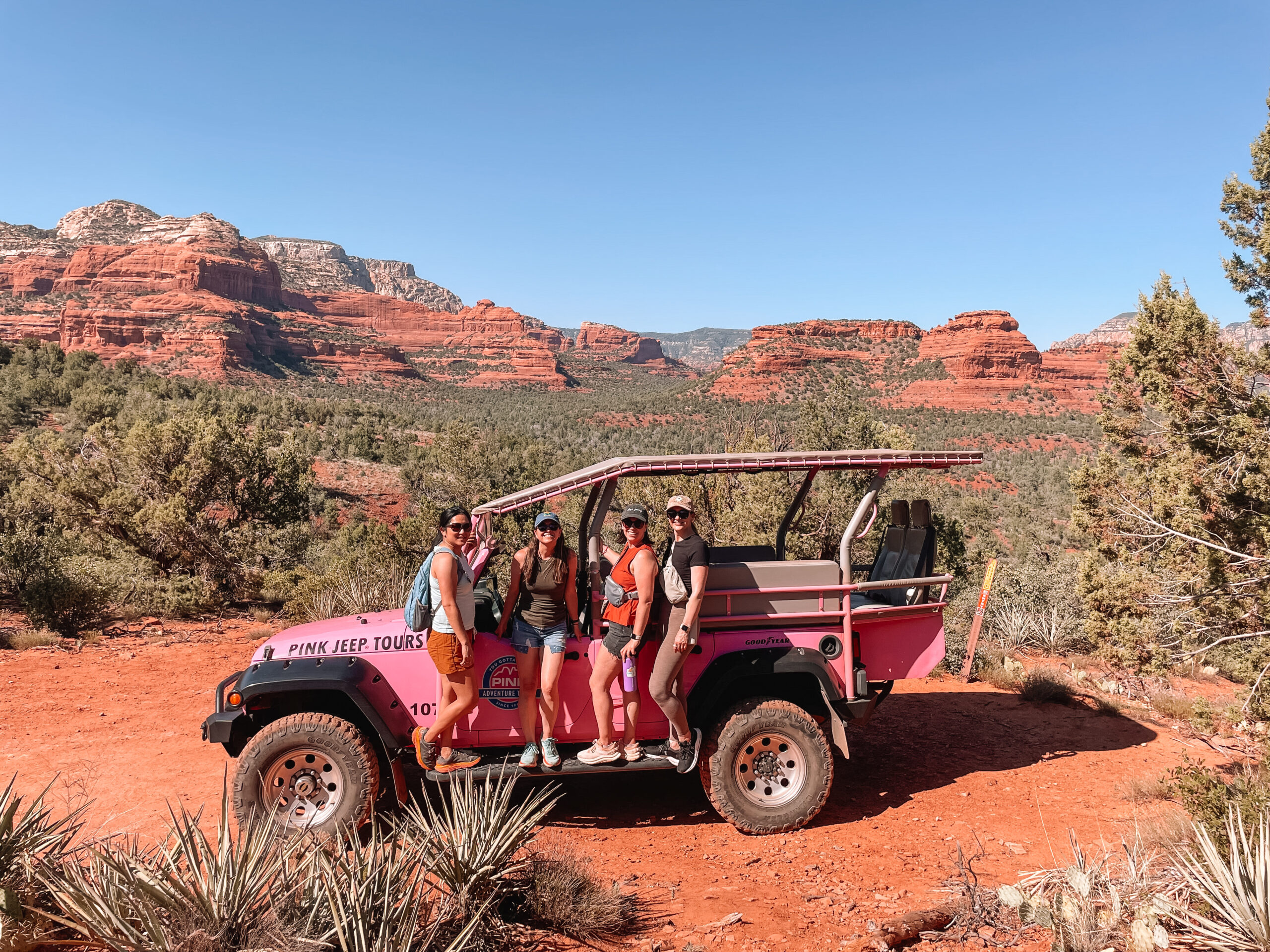 Pink Jeep Tour vehicle driving through rugged red rock terrain in Sedona, Arizona with dramatic cliffs and desert landscape in the background